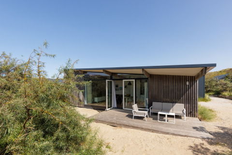Moderne Sea Lodges Bloemendaal 3 met houten buitenkant, terras en tuinmeubelen onder blauwe hemel.