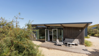 Moderne Sea Lodges Bloemendaal 3 met houten buitenkant, terras en tuinmeubelen onder blauwe hemel.