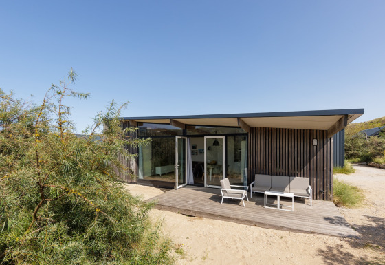 Moderne Sea Lodges Bloemendaal 3 met houten buitenkant, terras en tuinmeubelen onder blauwe hemel.