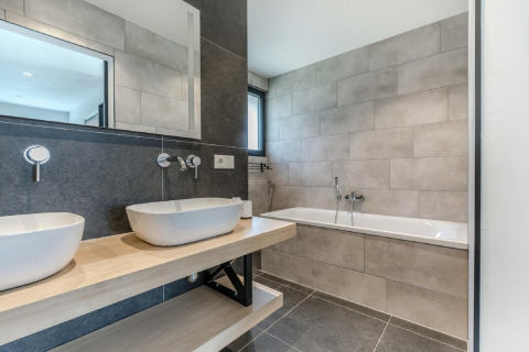 Baño moderno con doble lavabo, bañera y azulejos claros en el chalet Park de Kievit 19 de Bélgica.