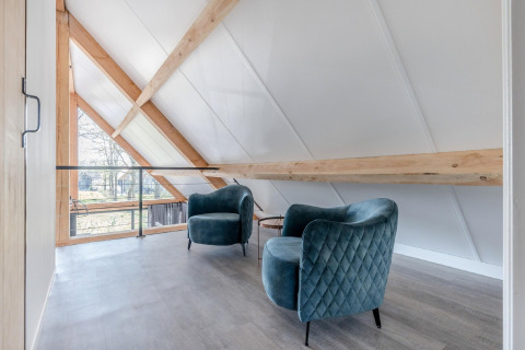 Heller Loftbereich im Chalet Park de Kievit 19 mit zwei blauen Sesseln und Holzbalken, Belgien.