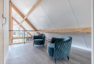 Luminoso altillo del chalet Park de Kievit 19 en Bélgica con dos sillones azules y vigas de madera.
