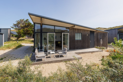 Moderne Sea Lodges Bloemendaal 1 met veel ramen, een terras en tuinmeubelen in een natuurlijke omgeving.