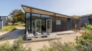 Moderne Sea Lodges Bloemendaal 1 met veel ramen, een terras en tuinmeubelen in een natuurlijke omgeving.