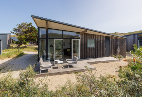 Moderne Sea Lodges Bloemendaal 1 met veel ramen, een terras en tuinmeubelen in een natuurlijke omgeving.