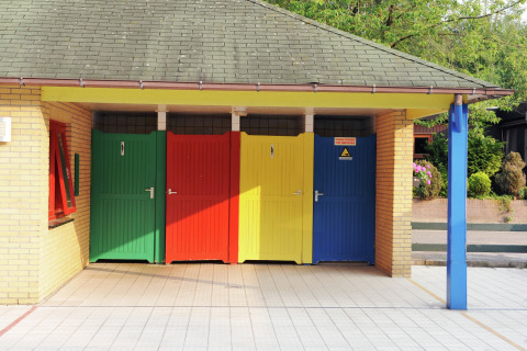 Bunte Türen eines Sanitärgebäudes bei einer Glamping-Unterkunft, umgeben von Natur und Außenbereich.