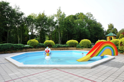 Piscina infantil en un chalet con una estatua de payaso y un tobogán arcoíris, rodeada de vegetación.