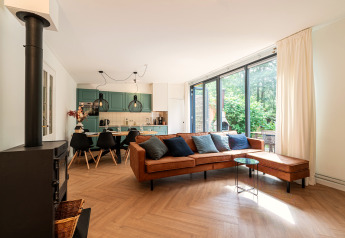 Modern living room at Wellness Suite lodge in the Netherlands with large windows and a brown leather sofa.