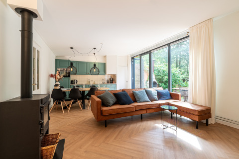 Moderne stue i Wellness Suite-lodge i Holland med lædersofa, stort vindue og åbent køkken.