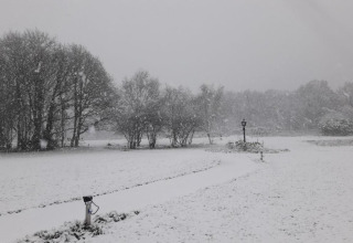 Alojamiento glamping cubierto de nieve, con árboles, faroles y senderos blancos en invierno.