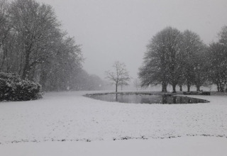 Ein glamping-Unterkunftsbereich im Winter, bedeckt mit Schnee, einem Teich und Bäumen im Schneefall.