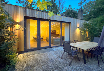 Buitenterras van Forest suite lodge met glazen deuren naar een warm verlichte woonkamer in het bos.