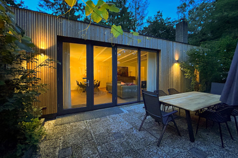 Outdoor patio of Forest suite lodge, showing glass doors to a warmly lit living room in a forest setting.