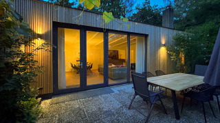 Abendliche Terrasse der Forest suite Lodge mit Glasfront und beleuchtetem Wohnzimmer im Wald.