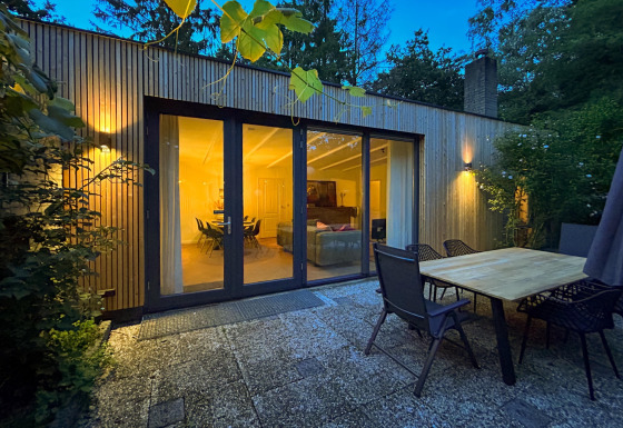 Udendørs terrasse ved Forest suite lodge i skoven, viser glasdøre til oplyst opholdsstue om aftenen.