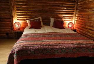 Acogedor dormitorio en un chalet de madera con cama doble, luz cálida y colcha colorida en Bélgica.