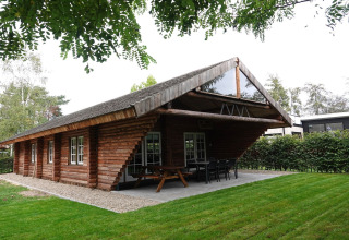 Træhytte ved Park de Kievit 11 i Belgien, med rummelig veranda, bord og stole, omgivet af grønt.