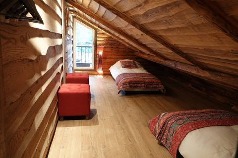 Ático del chalet Park de Kievit 11 en Bélgica con dos camas, pufs rojos y decoración de madera.
