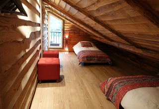 Ático del chalet Park de Kievit 11 en Bélgica con dos camas, pufs rojos y decoración de madera.