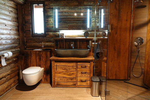 Rustikt badeværelse med træpaneler, fritstående vask, væghængt toilet og glasbruseniche i chalet.