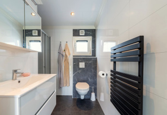 Moderne badeværelse med sort håndklædetørrer, bruser, toilet og håndvask i lodge Brabants Weelde 33.