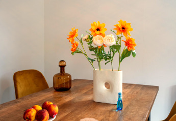 Bord med orange blomster i vase, ferskner, brun flaske og lille blå flaske på Brabants Weelde 33, Holland.