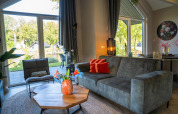 Sala moderna en Holiday Park «Latour 4» en los Países Bajos con grandes ventanas y vista al jardín.