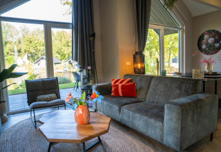 Salon moderne au Holiday Park «Latour 4» aux Pays-Bas avec de grandes fenêtres et vue sur le jardin.