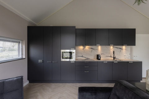 Modern kitchen with black cabinets, marble backsplash, and built-in appliances at Holiday Park Latour 4, Netherlands.