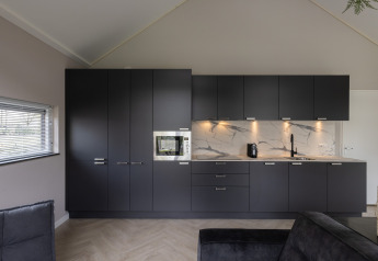 Cocina moderna con gabinetes negros, encimera de mármol y electrodomésticos en Holiday Park Latour 4, Países Bajos.
