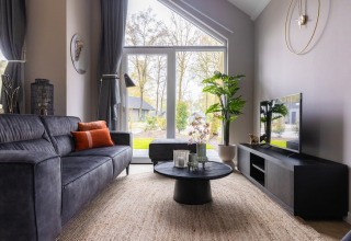 Modern living room at Holiday Park Latour 4, Netherlands, featuring large windows, a black sofa, and greenery.