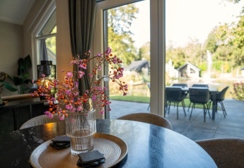 Moderne lodgeinteriør med blomsterdekoration og udsigt over en have gennem store vinduer i Holland.