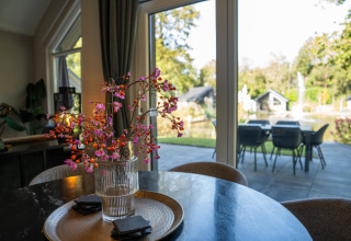 Modern lodge interior with glass vase flowers on table, opening onto patio and garden view in the Netherlands.