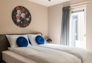 Soveværelse i Holiday Park «Latour 4» i Holland med dobbeltseng, blå puder og kunst på væggen.