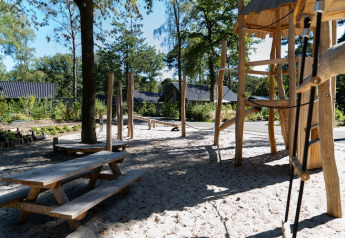 Natürlicher Spielplatz mit Holzmöbeln und Sand bei einer Lodge, umgeben von Bäumen und Ferienhäusern.