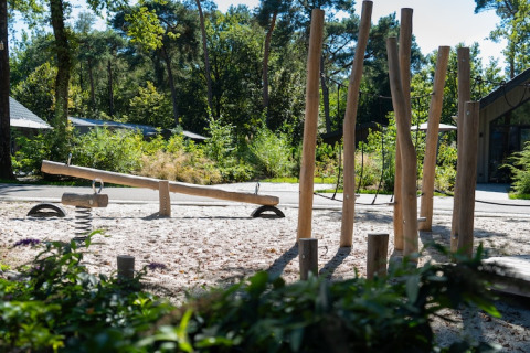 Aire de jeux extérieure près d’un lodge avec une balançoire à bascule, des poteaux en bois et nature.