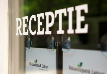 Ingang van de receptie met ‘RECEPTIE’ op de glazen deur bij Vakantiepark Latour, reflecties zichtbaar.