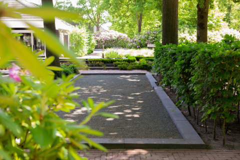 Scenic lodge garden with manicured hedges, flowerbeds, and shady trees under bright daylight.