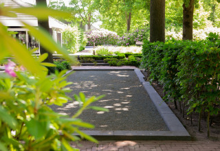 Scenic lodge garden with manicured hedges, flowerbeds, and shady trees under bright daylight.