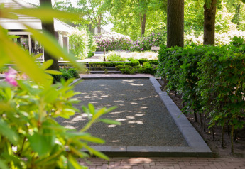 Gartenbereich einer Lodge mit gepflegten Hecken, Blumenbeeten und Bäumen an einem hellen Tag.
