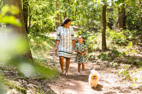 Une mère et sa fille promènent leur petit chien sur un sentier forestier près d’un lodge par beau temps.