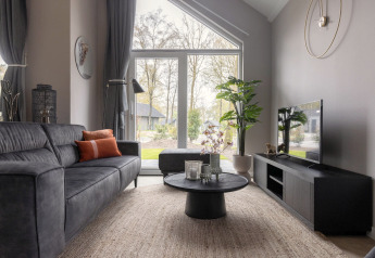 Moderne stue i Holiday Park «Latour 6» i Holland med stor glasdør, sofa og udsigt til natur.