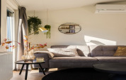 Moderne woonkamer in Holiday Park «Latour 8» met grijze bank, hangplanten en wanddecoratie in Nederland.