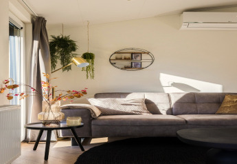 Moderne woonkamer in Holiday Park «Latour 8» met grijze bank, hangplanten en wanddecoratie in Nederland.