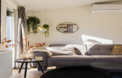 Modern living room at Holiday Park «Latour 8», grey sofa, plants, decorative shelves, natural light, Netherlands.