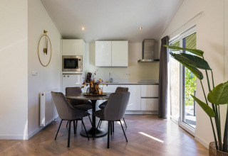 Moderne åbent køkken og spiseplads med grå stole, hvide skabe og store vinduer i Holiday Park Latour 8.