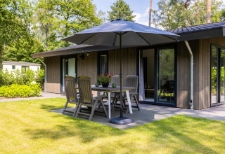 Sonnige Terrasse im Holiday Park Latour 8 in den Niederlanden mit Gartenmöbeln, Sonnenschirm und moderner Lodge.