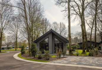 Moderne hytte i ferieparken Latour 6 i Holland, omgivet af træer og natur på en fredelig forårsdag.