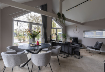 Moderne lodge med store vinduer, stue og spisehjørne med udsigt til naturen i Holiday Park Latour 6.