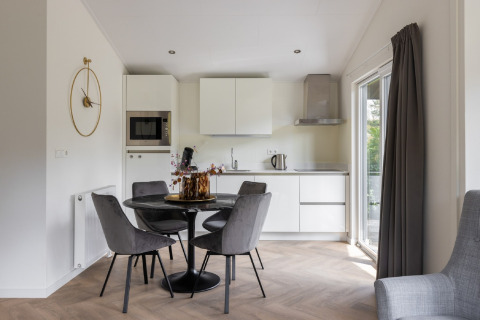 Moderne spise- og køkkenområde med grå stole og hvide skabe i Holiday Park «Latour 8», Holland.